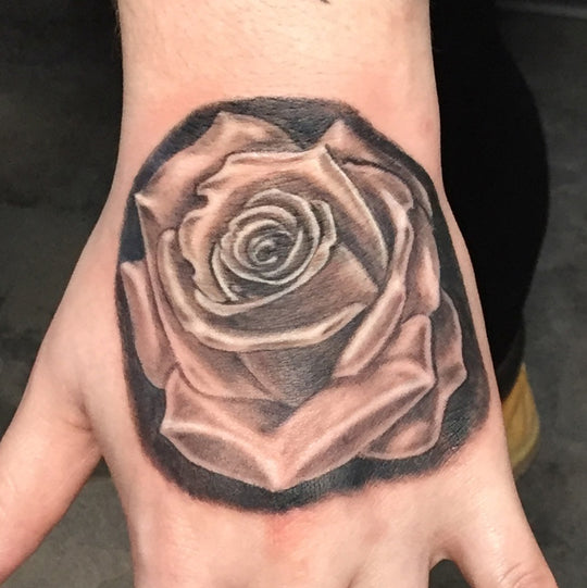A realistic black and grey rose tattoo on the back of a hand.
