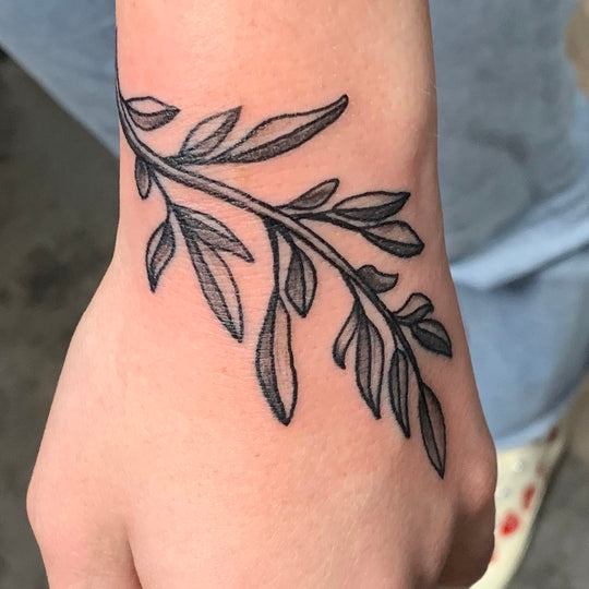 Black and grey leaves wrapping from a wrist to the top of a womans hand