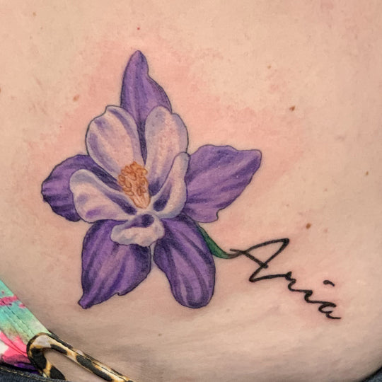 A purple and white columbine flower  tattoo with the stem forming the name Aria