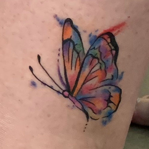 A small watercolor style butterfly tattoo on a woman's ankle