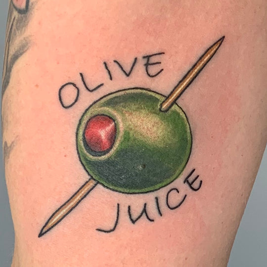 Neo traditional style tattoo of an olive with a toothpick through it and the words olive juice.