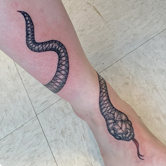 A black dot work snake wrapped around a girls lower leg with the head at the top of the foot.