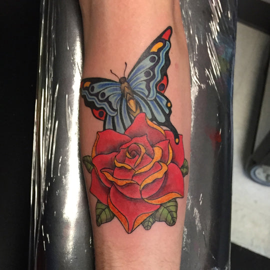 A tattoo of a blue butterfly and a red rose in a neo traditional style.