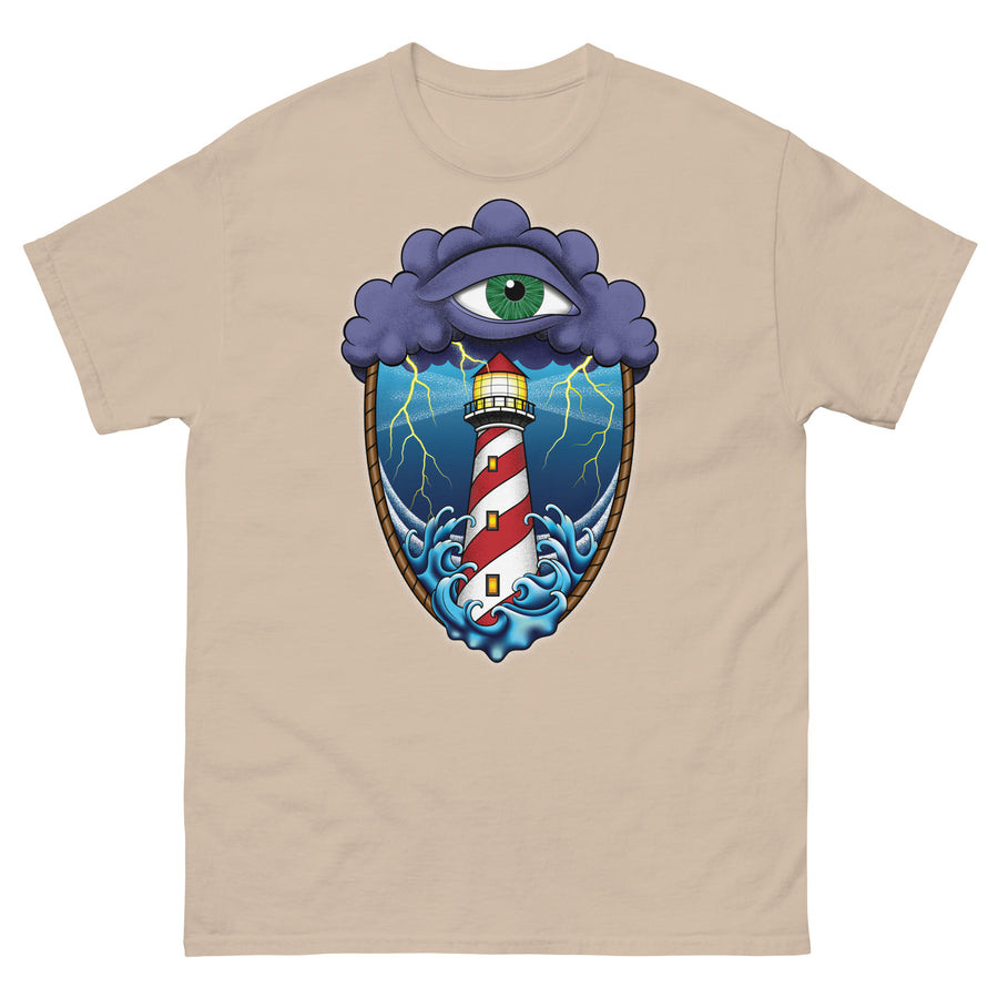 A sand brown t-shirt with an old school eye of the storm tattoo design of large dark purple storm clouds at the top of the design with a green eye in the middle of the clouds.  Below the clouds is an oval shape with brown rope. Inside the rope are stormy seas and a lighthouse with lightning striking in the background.  At the bottom of the design, some of the waves are spilling out of the rope barrier. The sky and seas are hues of blue; the lighthouse is white and red striped like a barber pole.