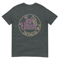 A dark grey t-shirt with a gold circle containing fancy lettering in purple and gold that says Ink Union and a gold tattoo machine peeking out from behind on the right side. There is a dot work gradient inside the circle, and the words Tattoo Co. in gold are at the bottom of the design.
