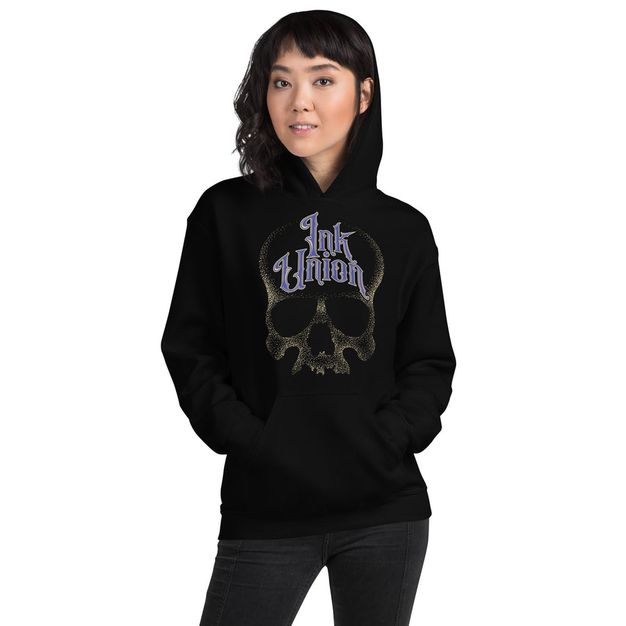 An attractive woman wearing a black hoodie adorned with a gold dot work human skull and the words Ink Union in fancy gold and blue lettering across the forehead of the skull.