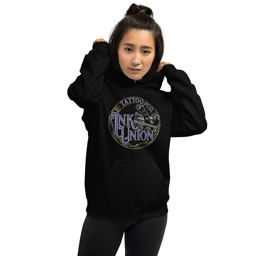 An attractive woman wearing a black hoodie  adorned with the Ink Union Tattoo Co. blue and gold with a silver tattoo machine logo.