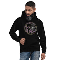 An attractive man wearing a black hoodie  adorned with the Ink Union Tattoo Co.  purple and gold with a silver tattoo machine logo.