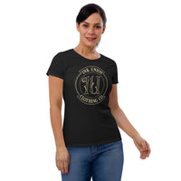 An attractive woman is wearing a black t-shirt adorned with the Ink Union Clothing Co gold badge logo containing fancy lettering and dot work gradients.