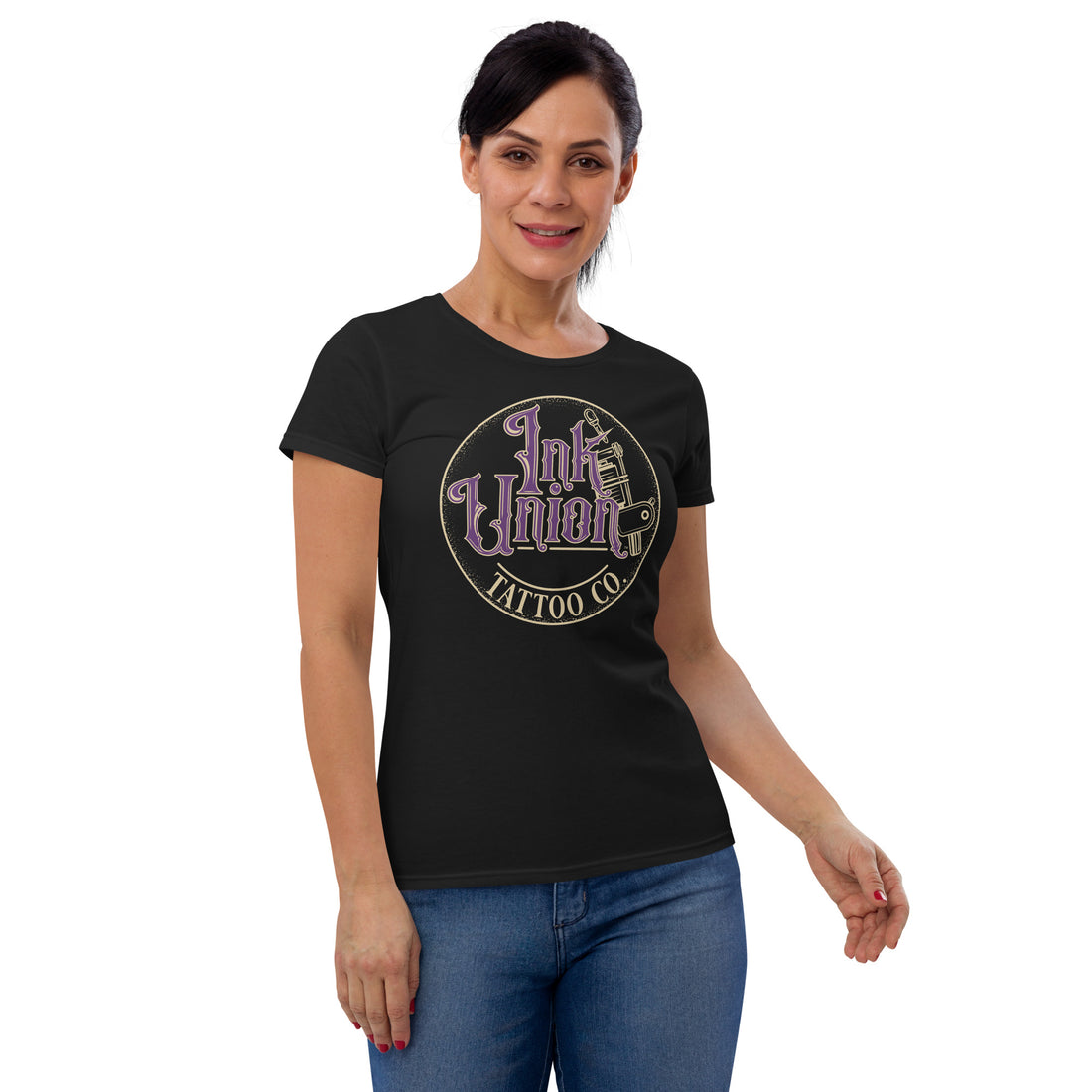 An attractive woman wearing a black t-shirt with a gold circle containing fancy lettering in purple and gold that says Ink Union and a gold tattoo machine peeking out from behind on the right side.  There is a dot work gradient inside the circle, and the words Tattoo Co. in gold are at the bottom of the design.