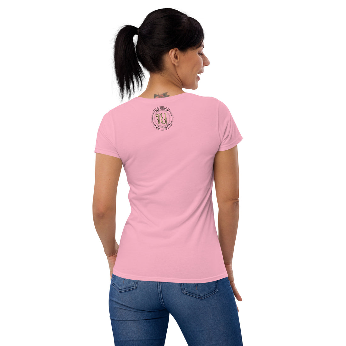 The rear view of an attractive woman wearing a pink t-shirt with a small gold and black Ink Union badge logo centered just under the neckline. 